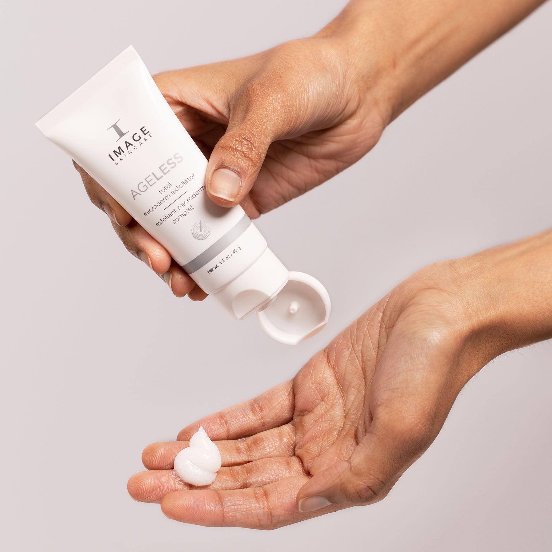 model hands holding ageless exfoliator pouring drop of exfoliator onto palm