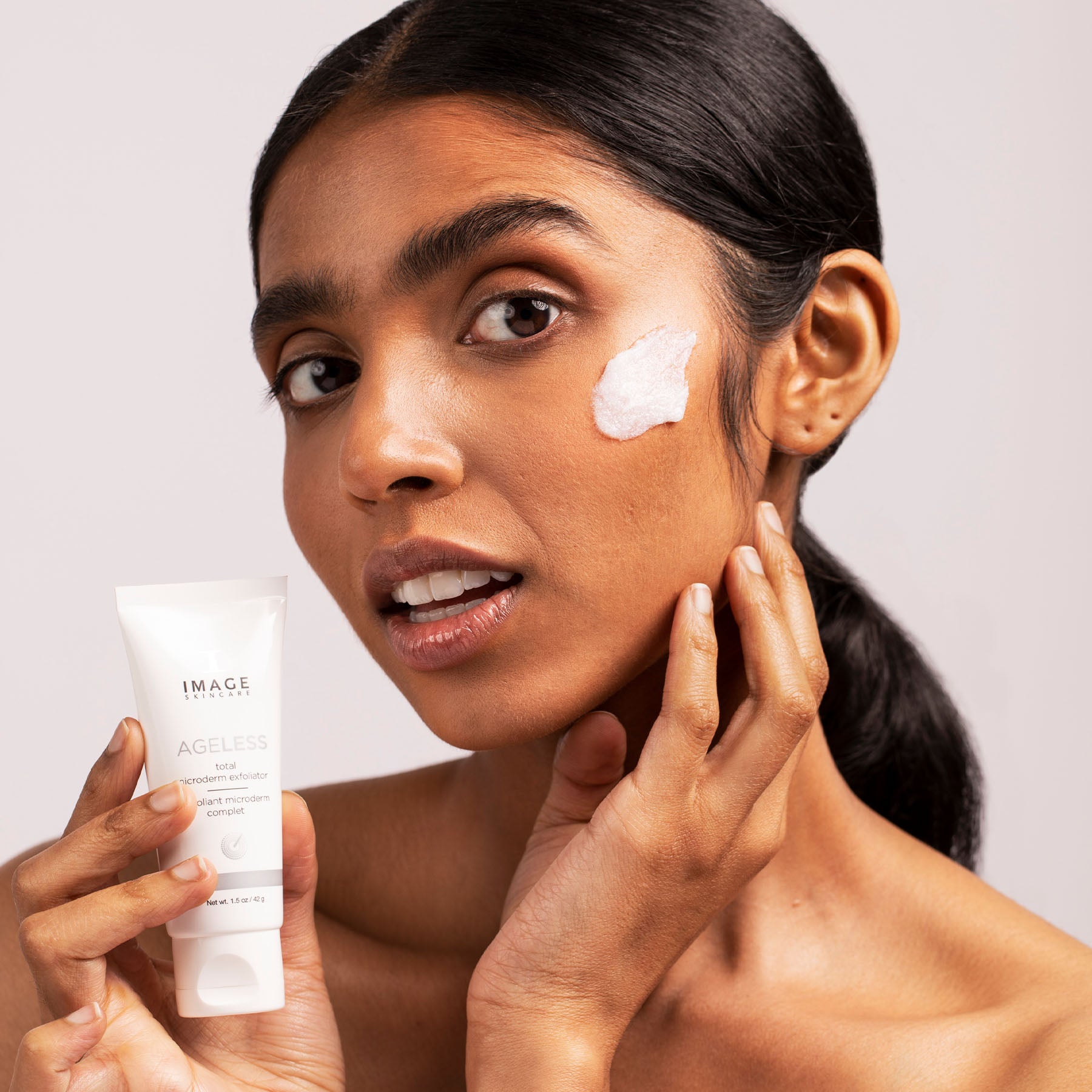 model holding product bottle applying exfoliator on face