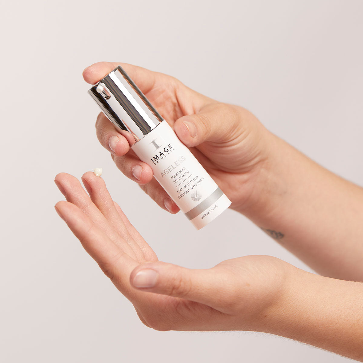 model hands holding product bottle and applying creme dot to finger