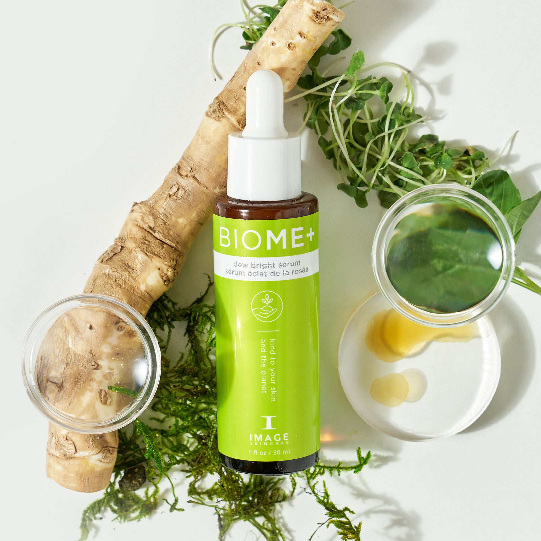 Biome+ dew bright serum bottle laid in between petri dishes with ingredients and plant leaves