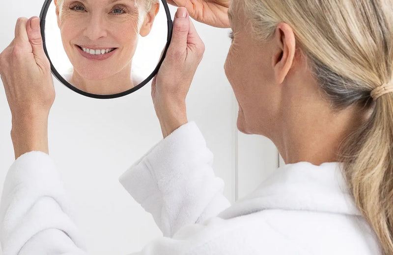 woman holding up mirror to face and smiling in reflection