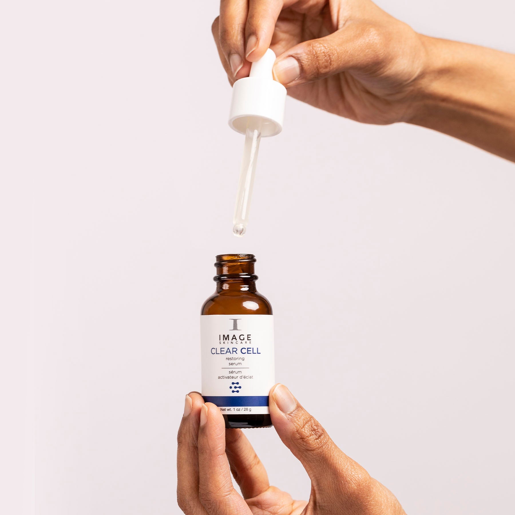 model hands holding open clear cell restoring serum bottle and holding applicator above bottle