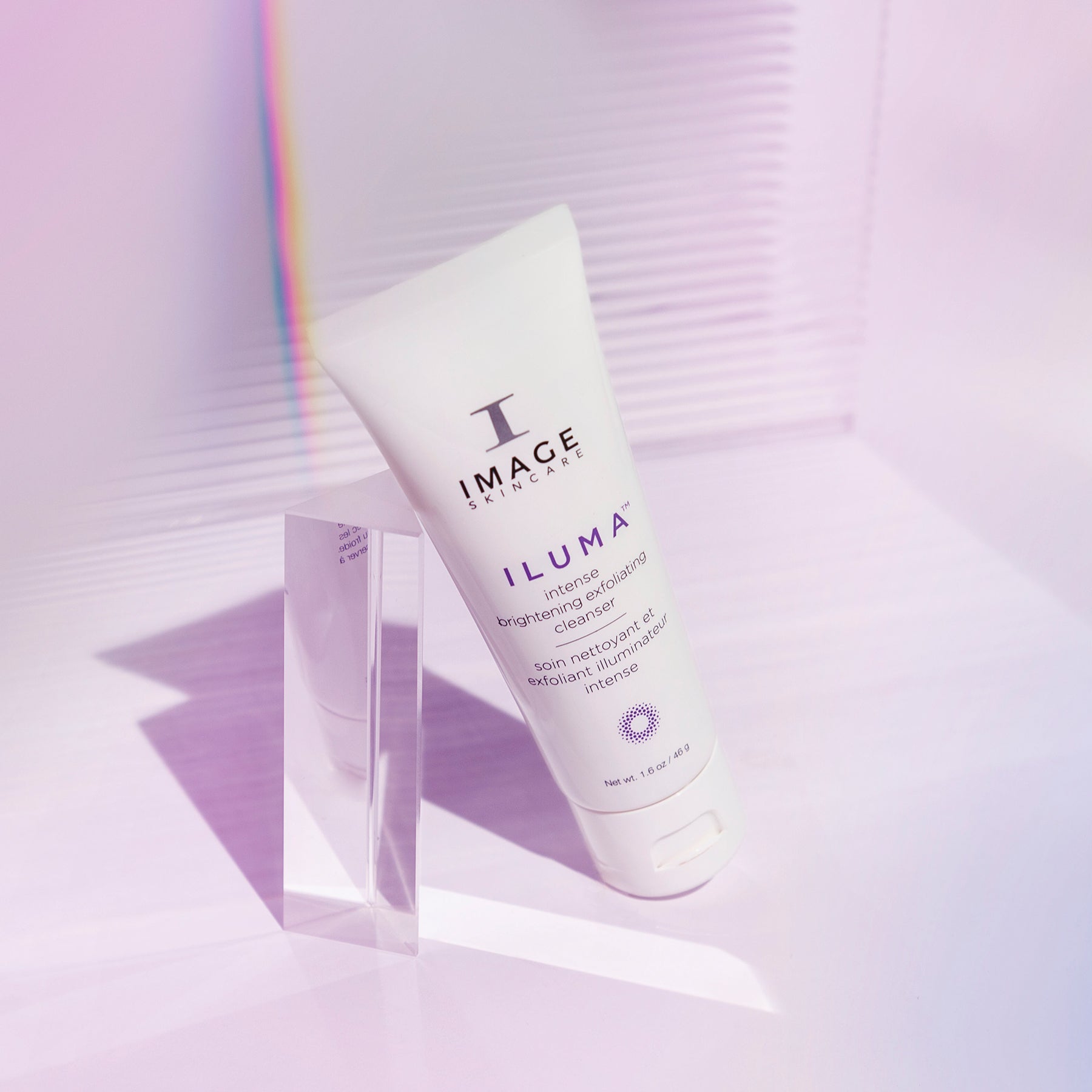 iluma cleanser travel size tube leaning against a prism on a light purple background