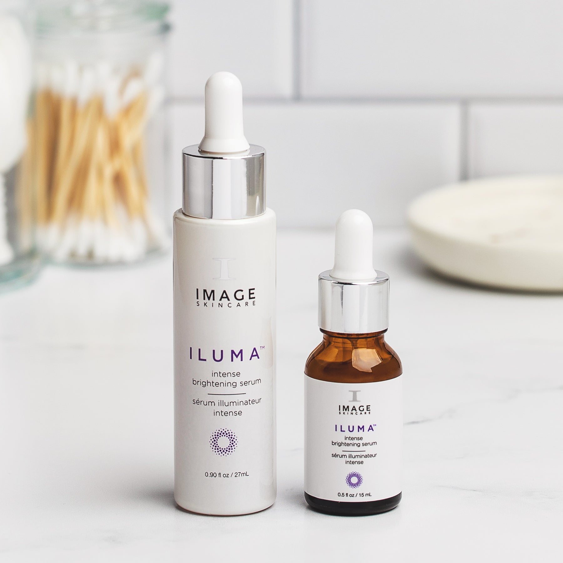 retail and travel size bottles of iluma brightening serum on a bathroom counter