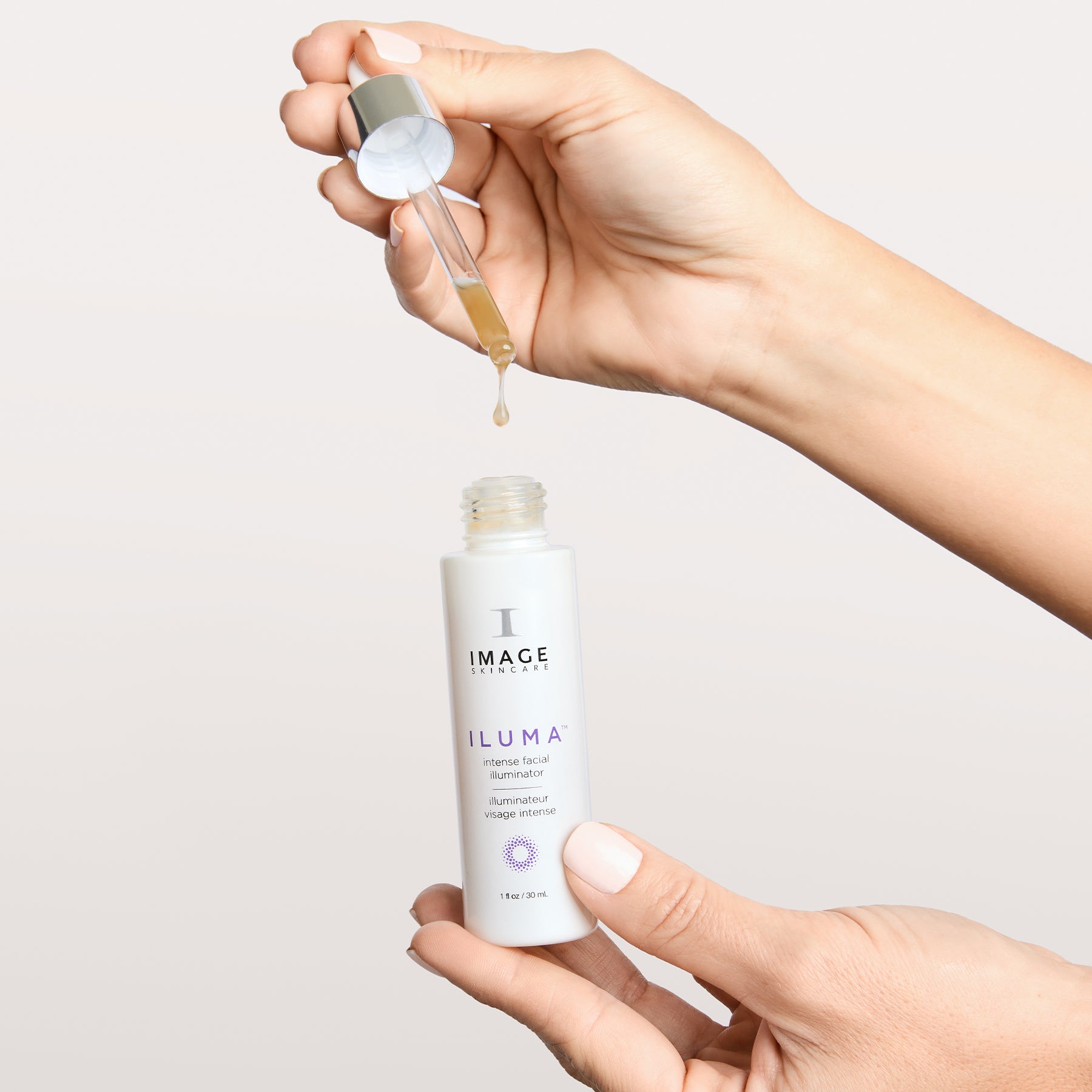 model hands holding illuminator bottle and dispensing serum from applicator