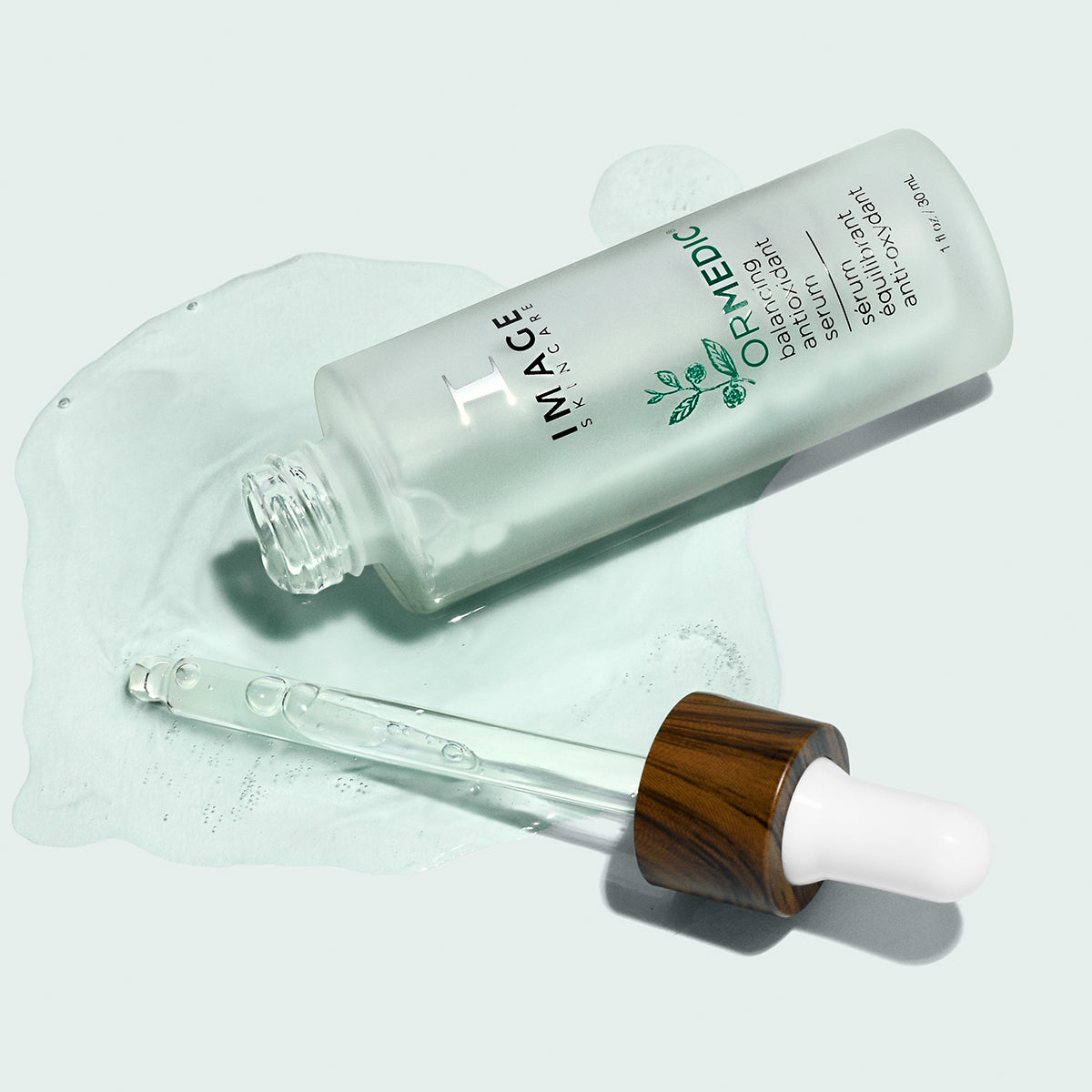 An open bottle of ORMEDIC antioxidant serum with product spilling out on light background