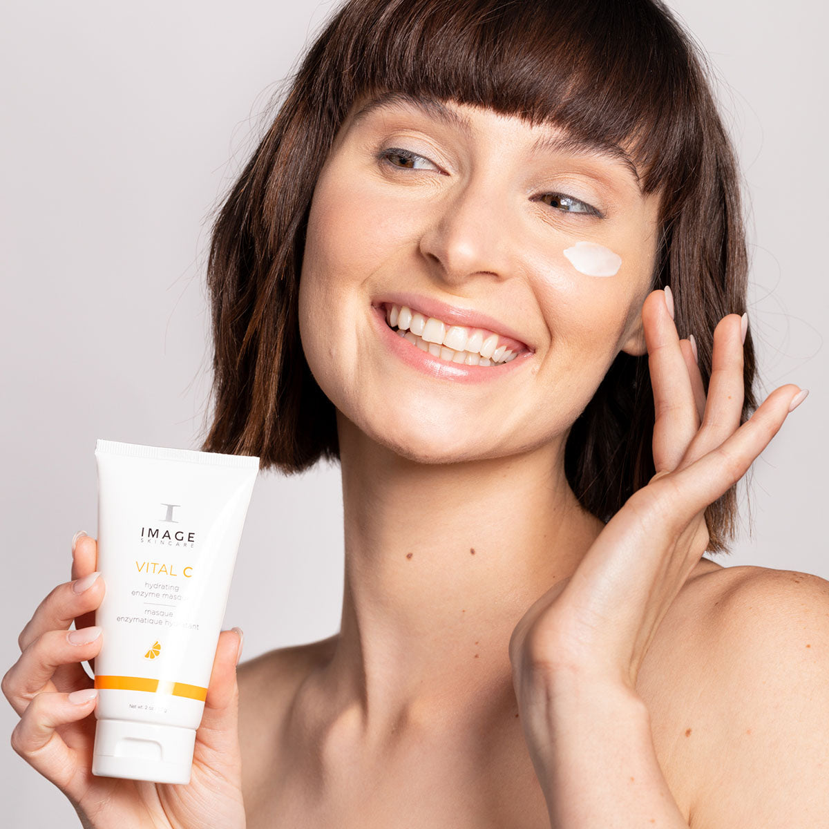 model holding enzyme masque with a masque applied on her cheek