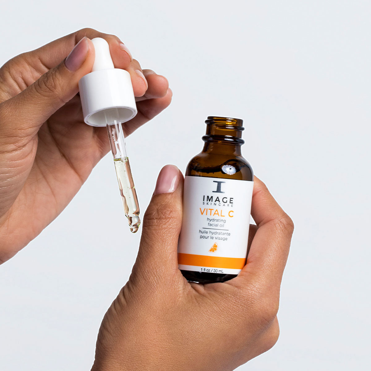 model hands with open facial oil bottle with dropper applying oil to hand