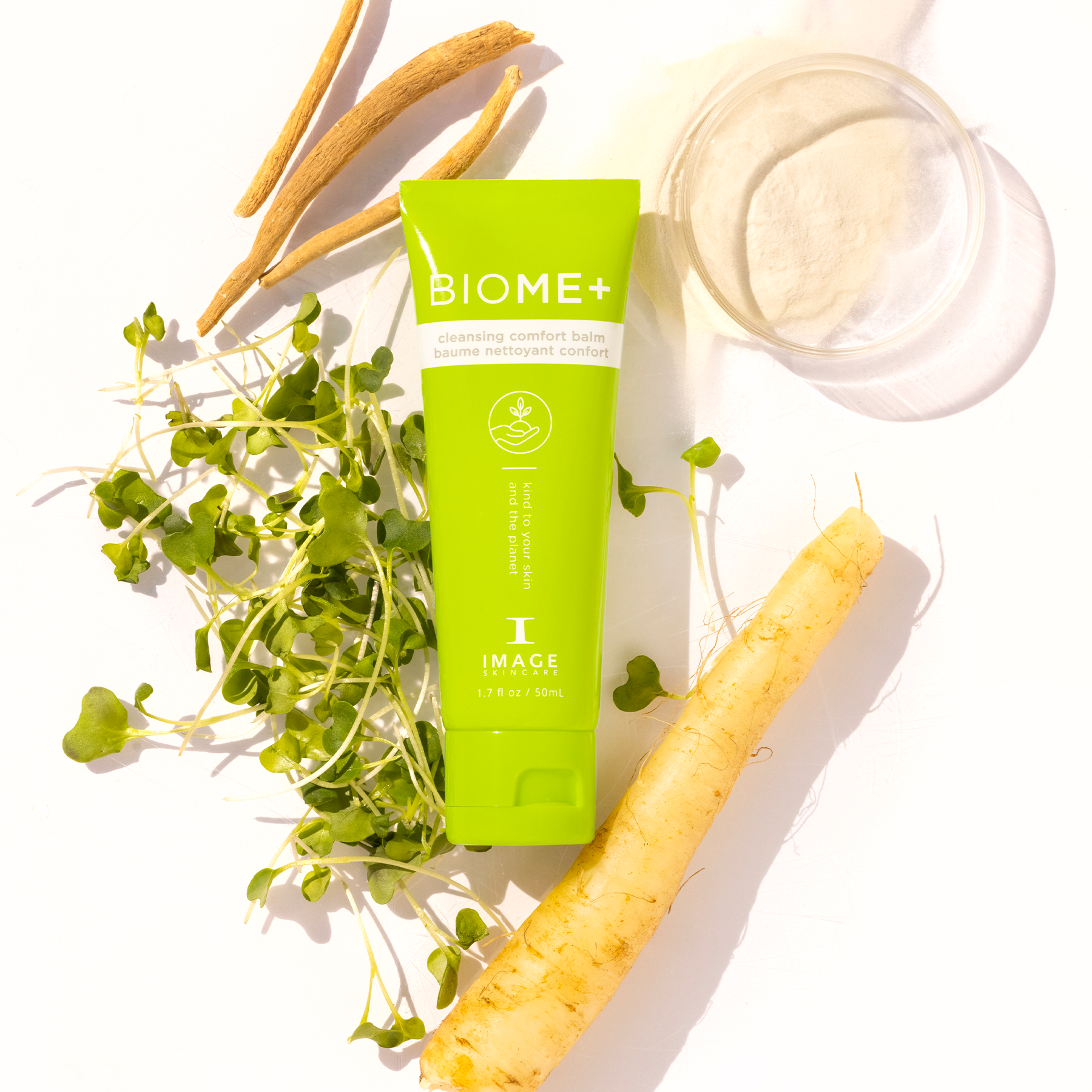 Biome+ cleansing comfort balm tube laid in between petri dishes with ingredients and plant leaves